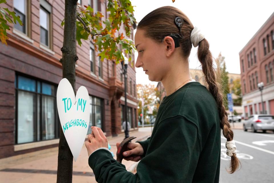 Miia Zellner, an art teacher from Turner, Maine, attaches a heart cut-out with a message of positivity to a tree in downtown Lewiston, Maine, Thursday, Oct. 26, 2023. Zellner wanted to show her love and support for the community in the wake of Wednesday's mass shootings. (AP Photo/Robert F. Bukaty)