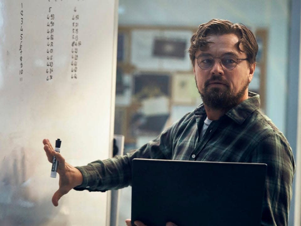 Leonardo DiCaprio holding a computer next to a white board