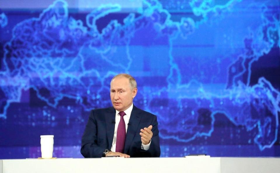 A handout image shows President Vladimir Putin, sitting and gesturing with one hand and sitting in front of a blue stylised world map as he takies part in an annual televised phone-in with the country's citizens dubbed "Direct Line with Vladimir Putin"  on June 30, 2021.