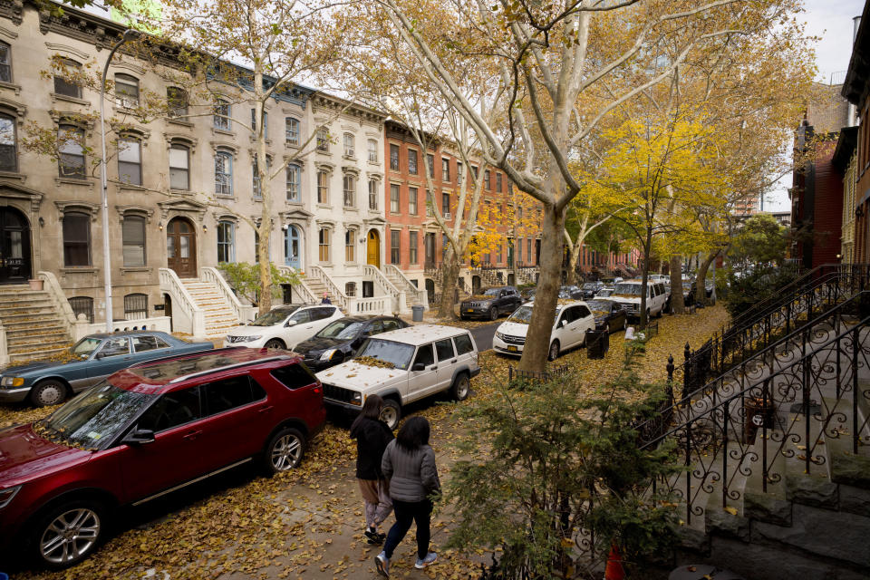 FILE- In this Wednesday, Nov. 7, 2018, file photo leaves cover cars and sidewalks on a tree-lined residential block in Long Island City in the Queens borough of New York. On Tuesday, Nov. 13, Amazon said it will split its second headquarters between Long Island City in New York and a suburb of Washington, in Arlington, Va. An expansion of that scope in a major city such as New York may seem like something a transit system could absorb. But some fear the addition of more commuters on already overcrowded roads and trains will just add to commuters’ headaches where Amazon makes its new homes. (AP Photo/Mark Lennihan, File)