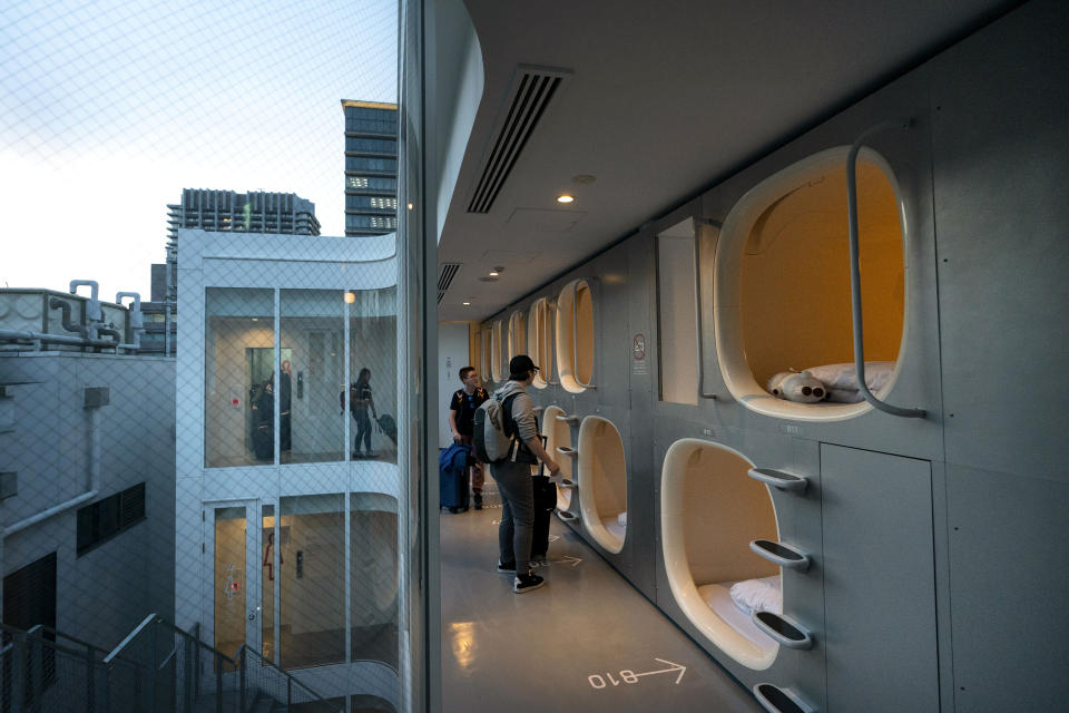 In this May 30, 2019, photo, a group of American tourists walk toward their pods after checking in at 9H capsule hotel at Chiyoda district of Tokyo. Tokyo is shaping up as a very pricey Olympics. Ticket demand is unprecedented, so scalping is sure to flourish. Hotel rates are soaring to five-six times normal. And getting here will be costly, particularly for fans from the Americas and Europe. (AP Photo/Jae C. Hong)