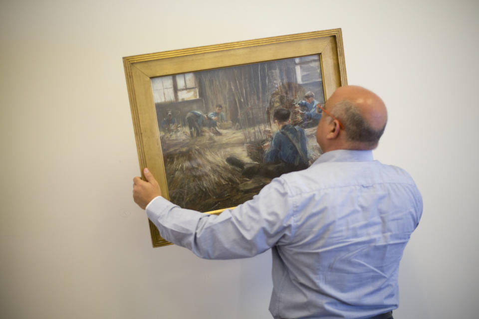 FILE - In this file photo taken on April 5, 2017, Meir Heller, the Jerusalem lawyer whose client then insisted on maintaining his anonymity holds Max Liebermann's "Basket Weavers" painting in a law office in Jerusalem. The painting was returned to David Toren, an American heir of its original Jewish owner, after he sued the government of Germany for his great-uncle’s collection and after a lengthy saga, recovered artworks confiscated by the Nazis, jockeyed by an unscrupulous German art trader and ultimately purchased by an Israeli Holocaust survivor unaware of its murky past. Toren died on April 19 in his Manhattan home from symptoms of the coronavirus. He was 94. He left behind his son Peter and two grandchildren. (AP Photo/Ariel Schalit, File)