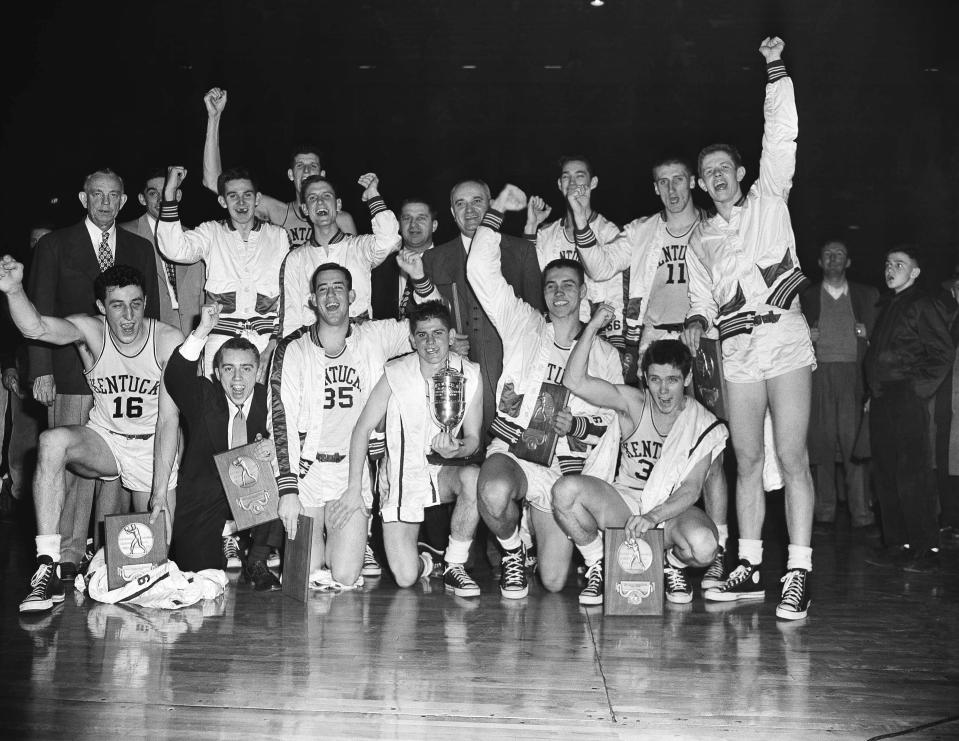 FILE - The Kentucky basketball team, which won the 1951 NCAA basketball championship, celebrates in Minneapolis, March 28, 1951, as it displays the team trophy and individual plaques. At center right is coach Adolph Rupp. Team members are, front row from left: Louis Tsioropoulos, C.M. Newton, Bobby Watson, Cliff Hagen, Lucian Whitaker and Frank Ramsey. Rear, from left: Dwight Price, Bill Spivey, Guy Strong, Roger Layne and Shelby Linville. (AP Photo/Chet Magnuson, File)