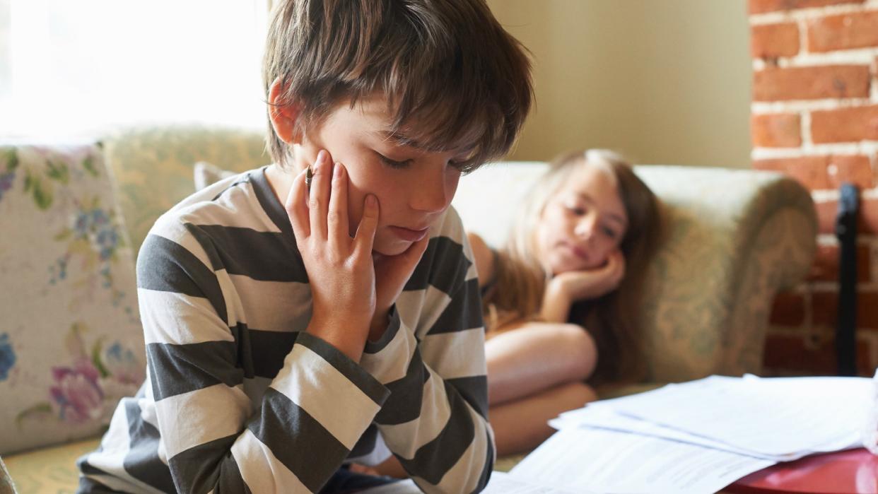  Two kids sitting on the couch at home studying school papers . 