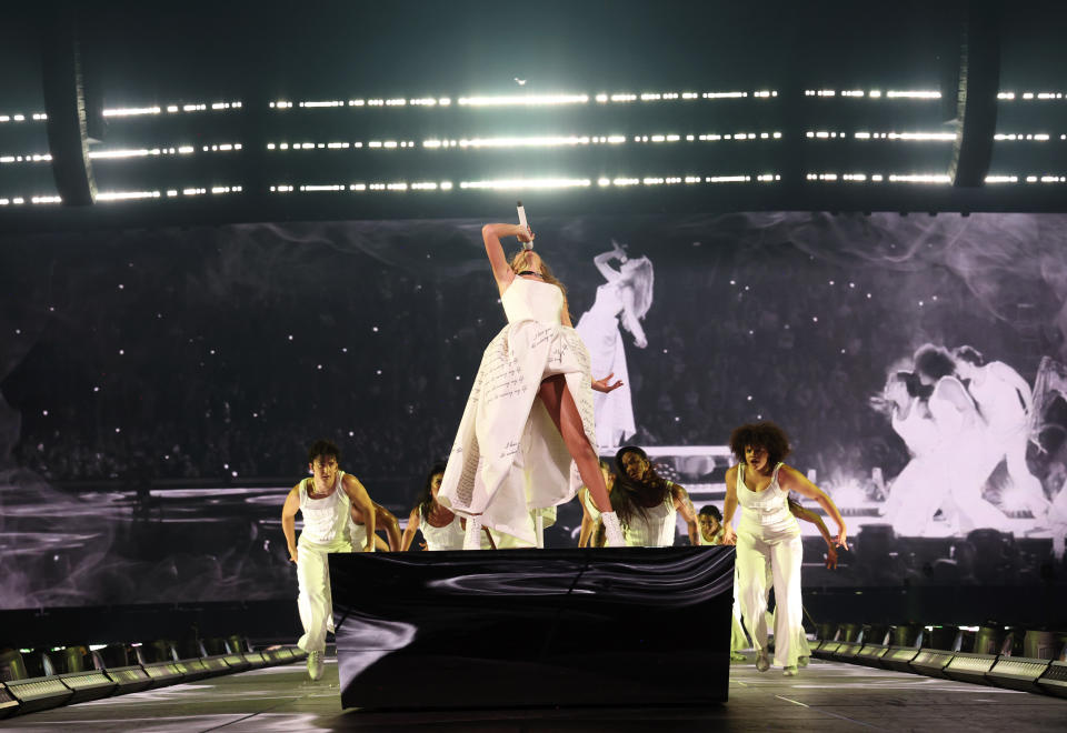 Taylor singing in a dramatic pose on her levitated platform with dancers behind her