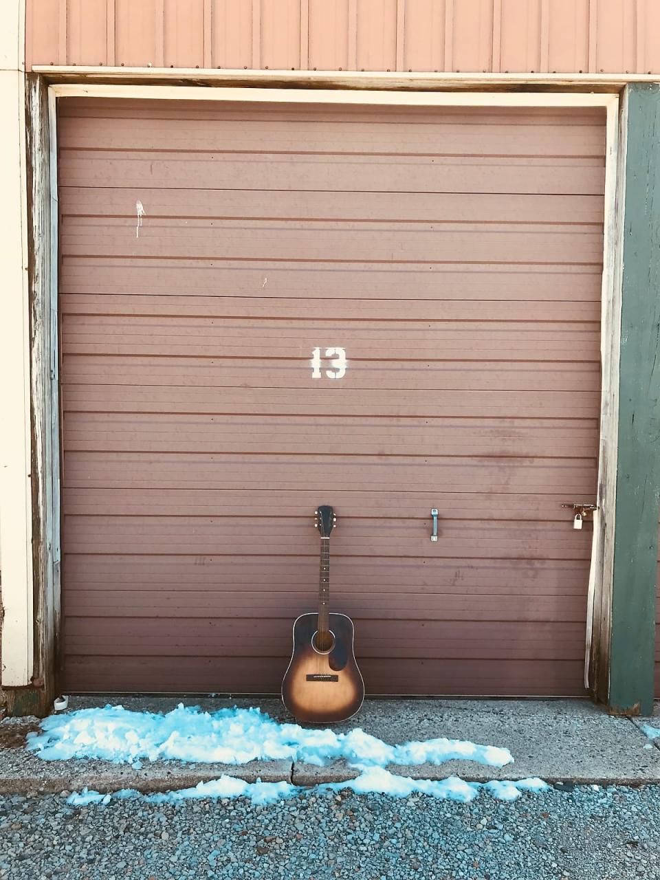 An acoustic guitar sits against a storage door with the number 13 on it