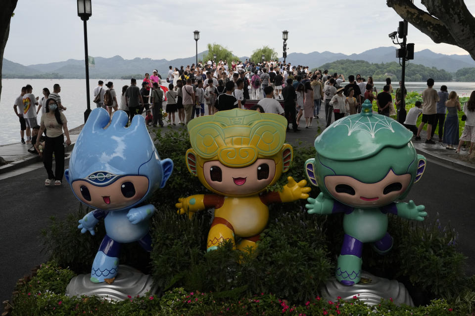 Tourists visiting the Westlake pass near official mascots of the 19th Asian Games in Hangzhou in eastern China's Zhejiang province, on June 26, 2023. The Asian Games open in two weeks, the first multi-sport international event in China since pandemic restrictions were lifted there about nine months ago. Unmatched for size, the Asian Games may even surpass the Olympics for controversy, power politics and intrigue. (AP Photo/Ng Han Guan)