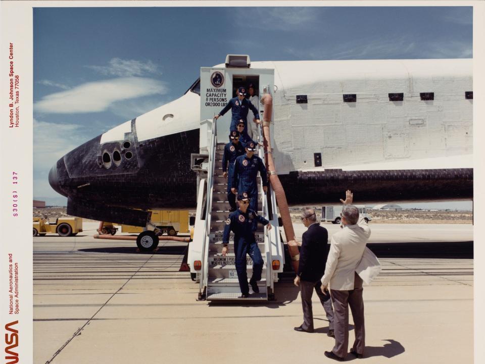 A aged photo shows a crew descending from an early space shuttle.