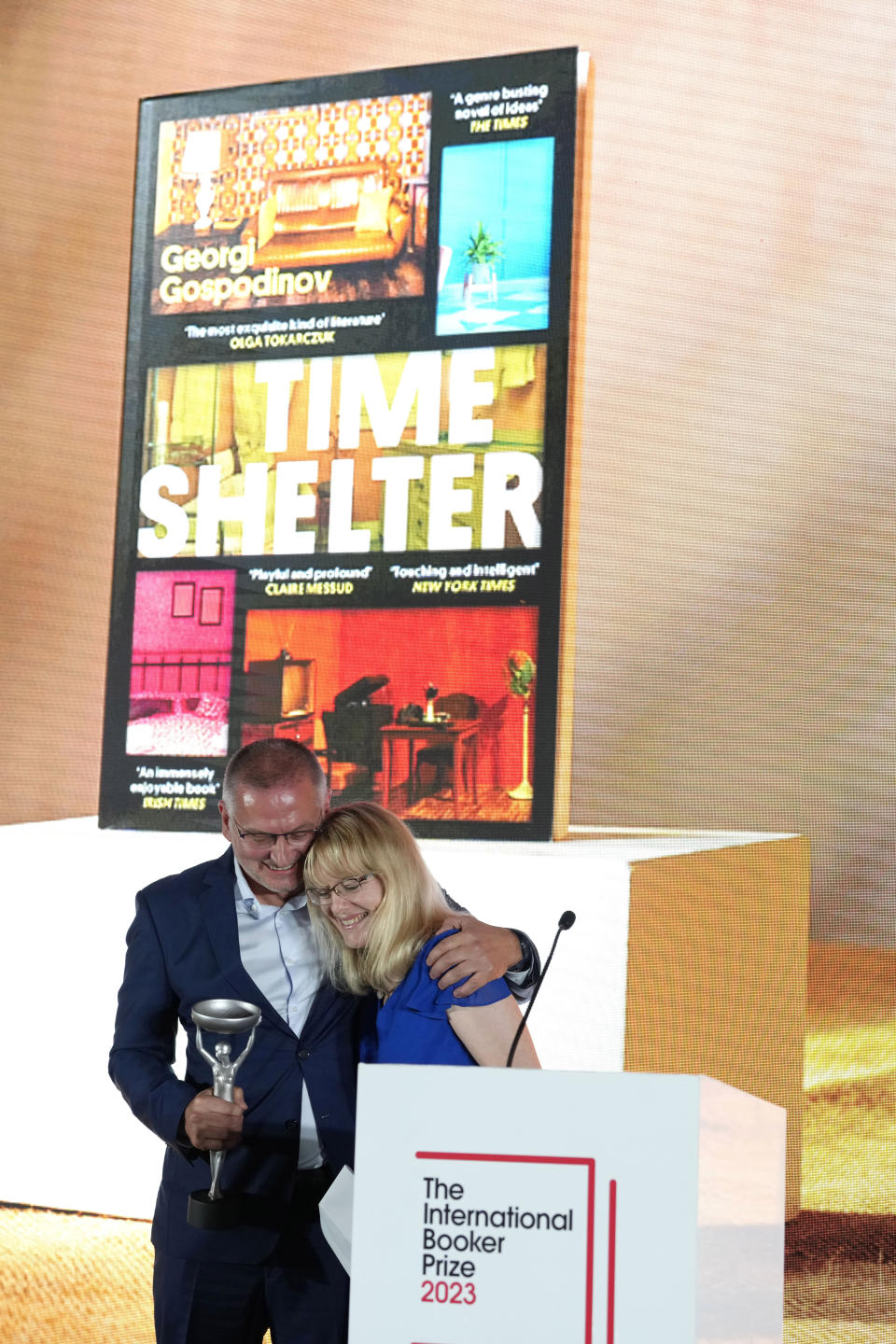 Bulgarian writer Georgi Gospodinov stands in front of a picture of his book "Time Shelter" translated from Bulgarian by Angela Rodel, right, after winning The International Booker Prize 2023, in London, Tuesday, May 23, 2023. (AP Photo/Kirsty Wigglesworth)