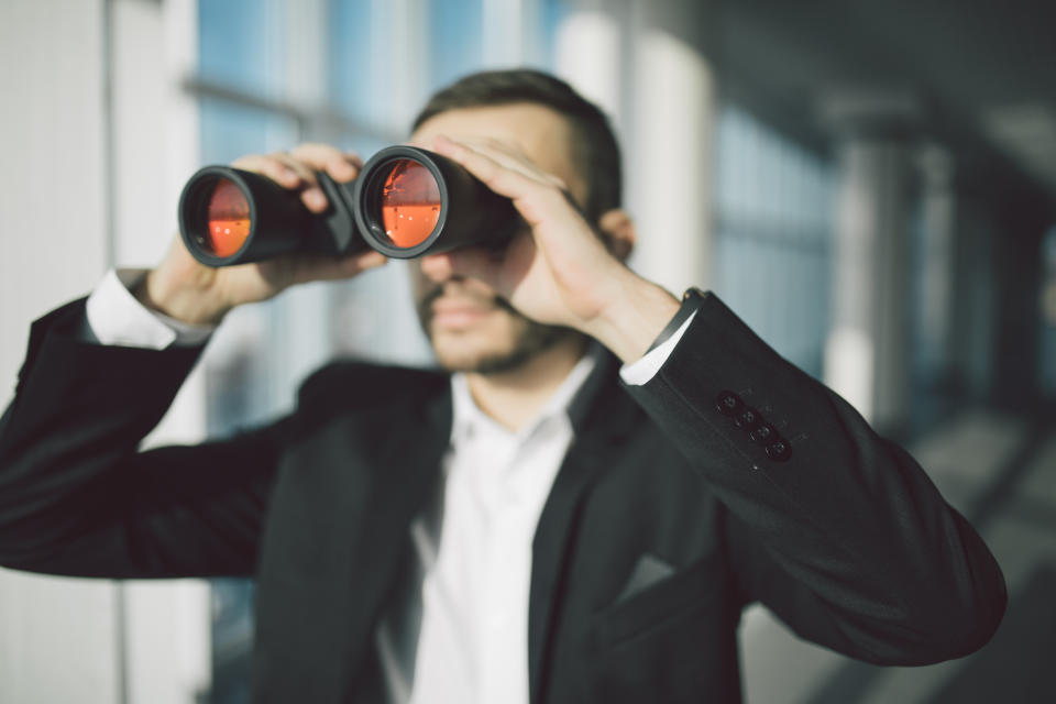 A man in a suit looking through binoculars.