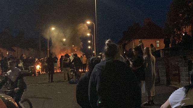 Police in riot shields are facing off against large crowds around a fire in Ely, Cardiff, hurling bricks and blazing items at them. The 