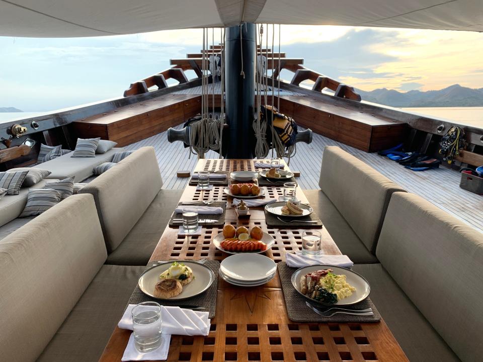 A table and seating area on the deck of a ship with plates set out for breakfast.