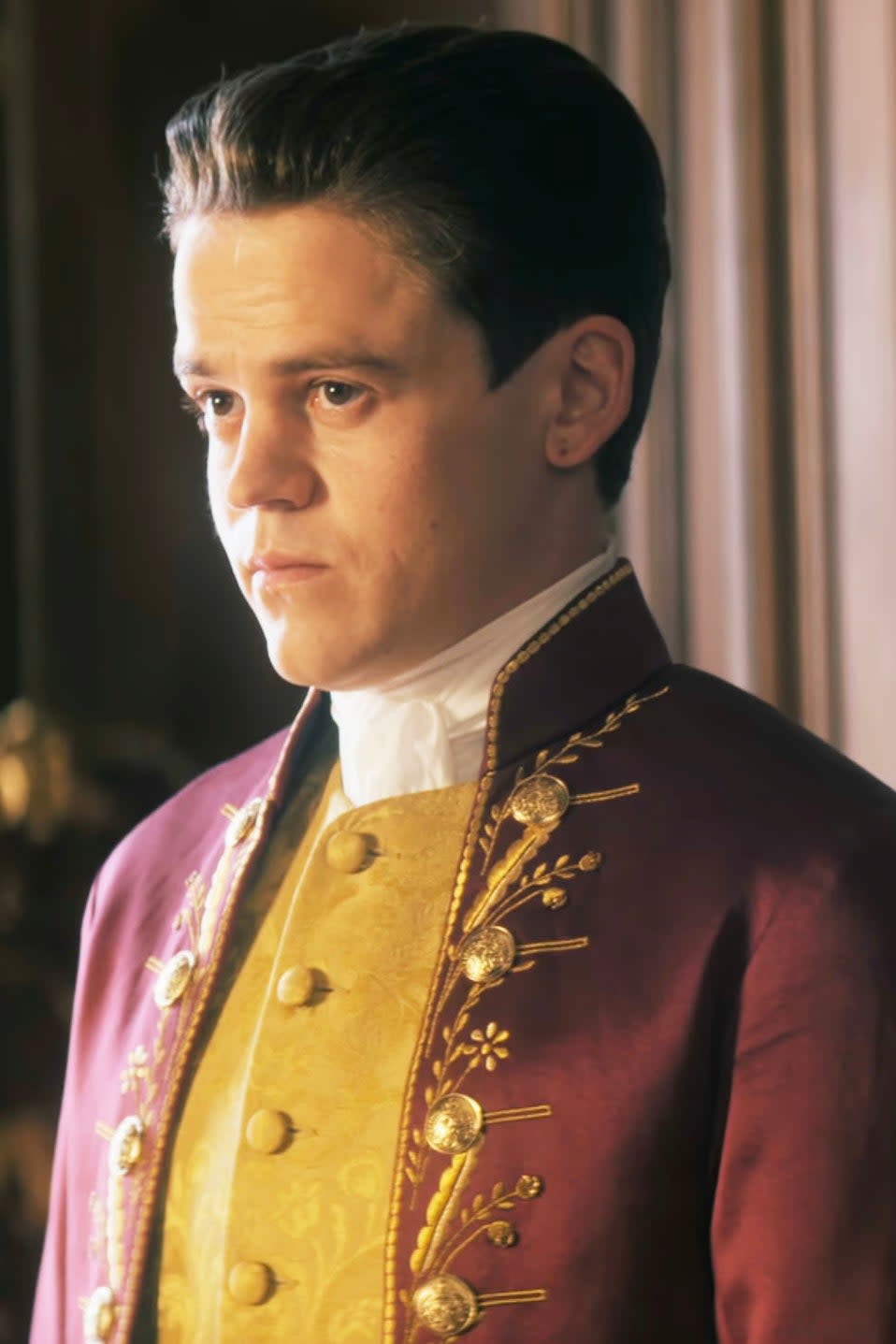 Sam Clemmett as young Brimsley in historical attire with gold embroidery, staring intently