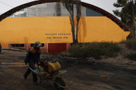 En esta imagen del 20 de enero de 2020, un hombre empuja una carretilla ante un recinto deportivo que lleva el nombre del expresidente Evo Morales, en Achocalla, Bolivia. Durante su mandato, a menudo Morales inauguraba personalmente los recintos deportivos jugando un partido de fútbol contra funcionarios locales. (AP Foto/Juan Karita)