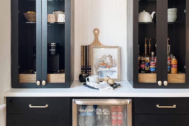 a black coffee bar with gold handles on the drawers and a pull out tray for the coffee maker, etc