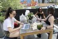 Natalie Boegel, left, Shianne Williams-Brwon and Caitlin McAfee talk while eating from a restaurant at the R. House food hall, Wednesday, July 15, 2020, in Baltimore. The hall, which houses a variety of restaurants, has modified its seating areas as well as implementing an order and pay by phone system to ensure contactless transactions between restaurant operators and customers. (AP Photo/Julio Cortez)