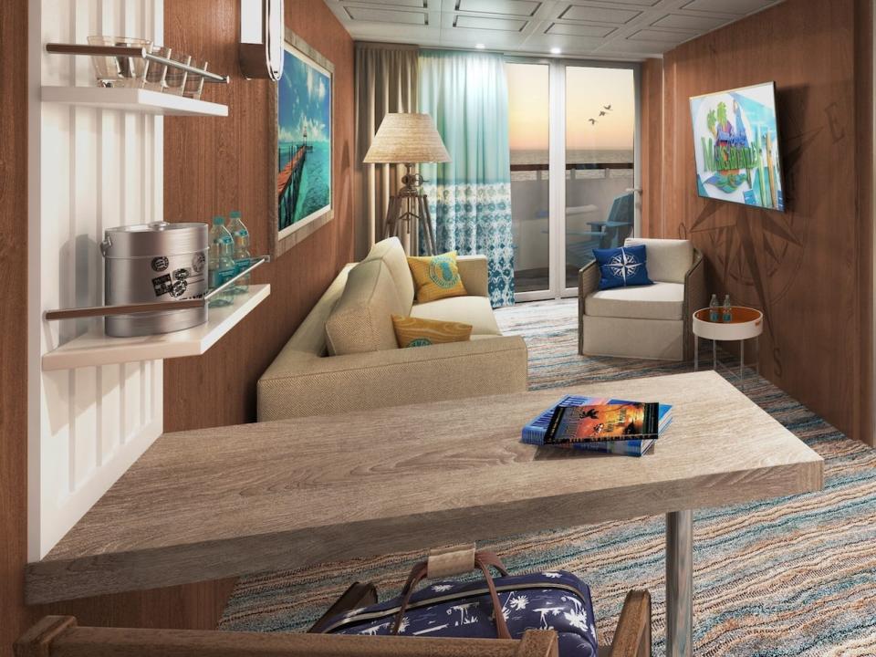 A suite aboard the Margaritaville Paradise with a couch, table, balcony, and bed in the corner