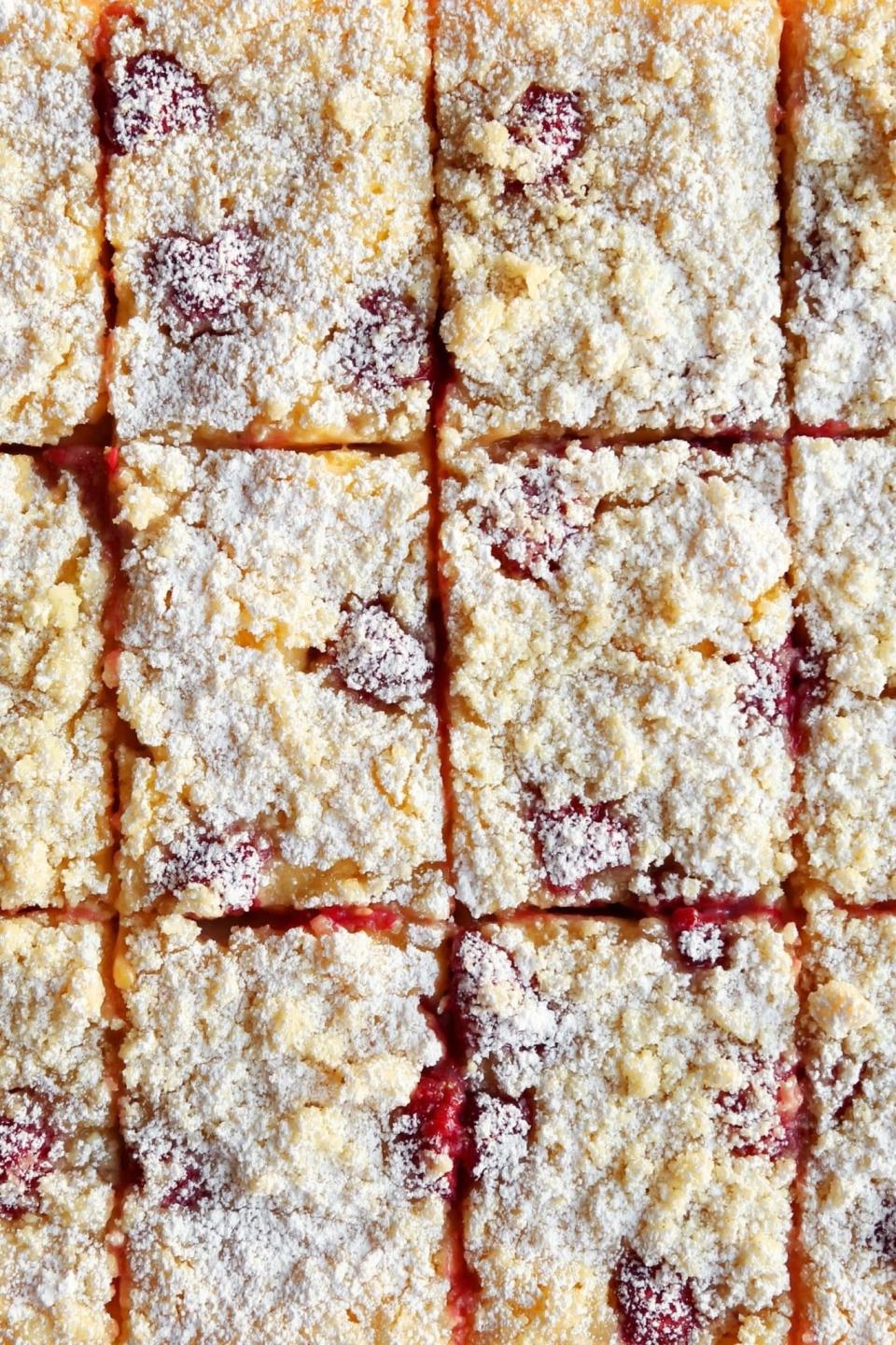 Close-up of squares of lemon raspberry bars with a powdered sugar topping and visible chunks of fruit