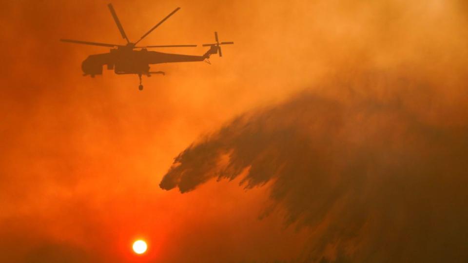 A firefighting helicopter makes water drop as a wildfire burns near the village of Metochi