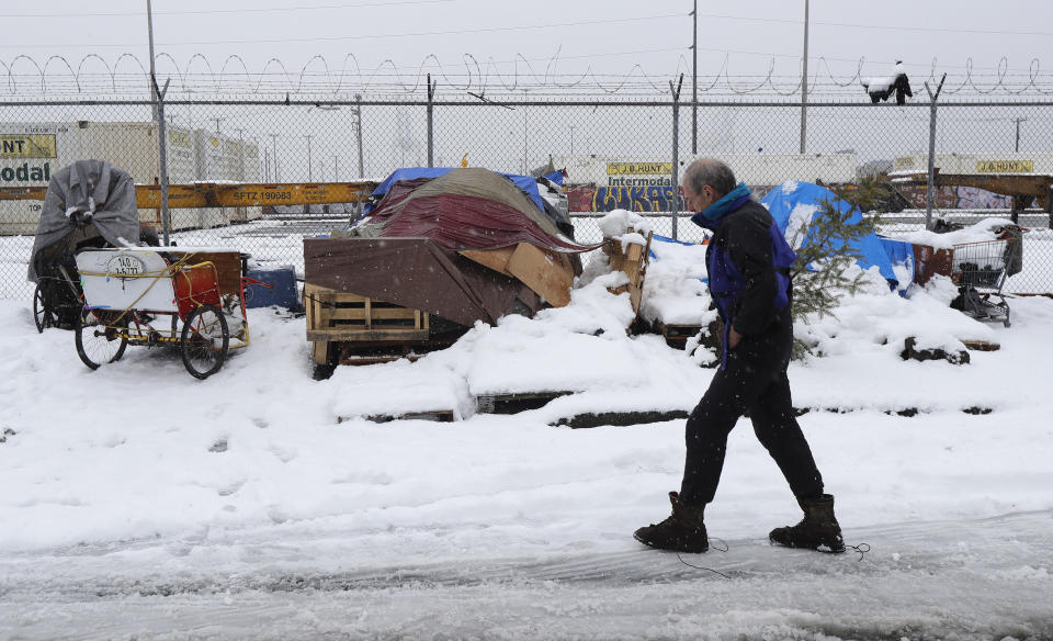 Kevin Shepherd walks back to the tent where he lives as snow falls in Seattle's SODO neighborhood, Monday, Feb. 11, 2019, in Seattle. Shepherd, who works as a musician and pedi-cab driver when the weather is better, said keeping warm is the hardest part of being unsheltered during the winter weather that has dumped snow across the Northwest. Seattle's metro area has already been hit by three snowstorms in February, making it the snowiest month in Seattle in more than 30 years. (AP Photo/Ted S. Warren)