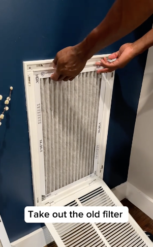 Person replacing an air filter in a wall vent, with text "Take out the old filter"