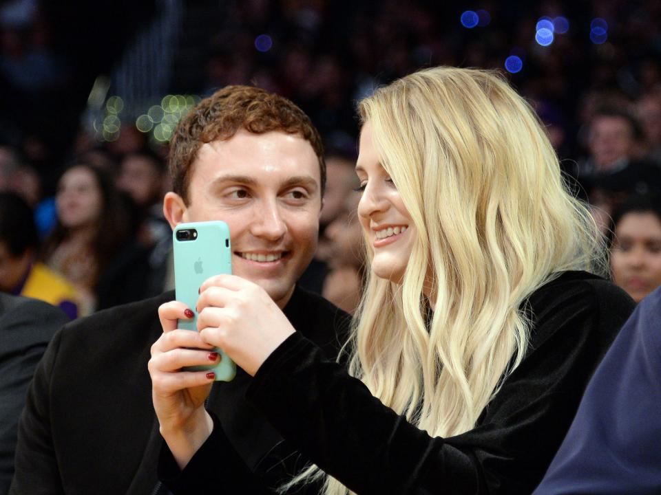 daryl sabara and meghan trainor at a lakers vs. clippers game. trainor is taking a photo of the court and smiling, while sabara is looking at her and grinning