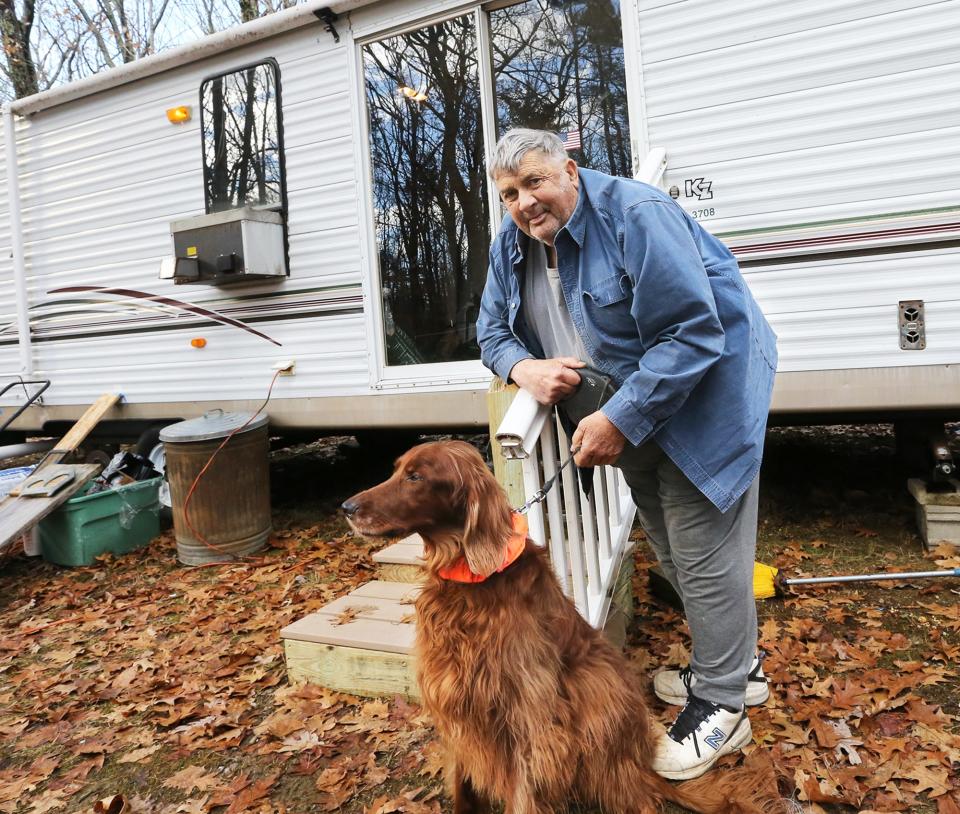 Tom Barr, a 76-year-old Vietnam veteran who received a Purple Heart and served as Eliot, Maine’s police chief, smiles with his dog, Rusty, in front of his cozy trailer with a pellet stove. He will live in the trailer until he gets a new mobile home, thanks to the donations of his community.