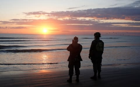 World War II reenactors stand looking out to sea on Omaha Beach, in Normandy, France, at dawn - Credit: AP