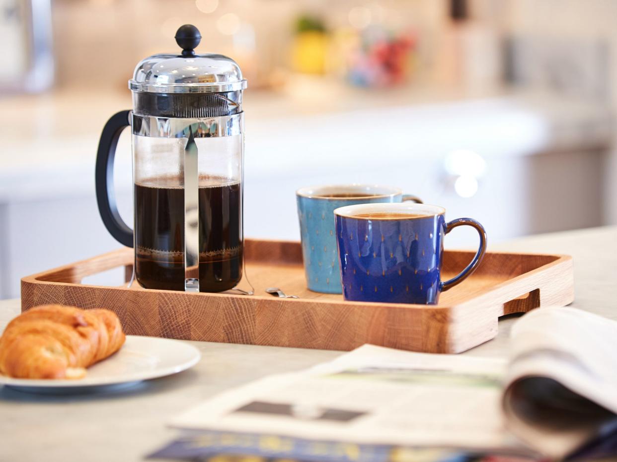 Coffee brewed in cafetiere on the kitchen work top with woman in background using sink