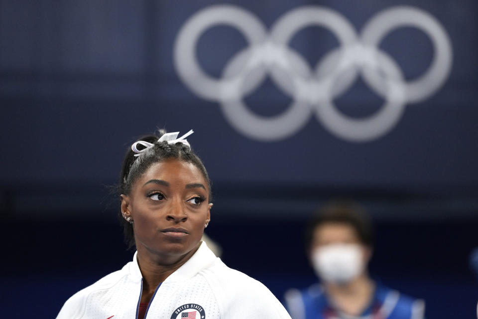 Simone Biles, of the United States, watches gymnasts perform after she exited the team final with apparent injury, at the 2020 Summer Olympics, Tuesday, July 27, 2021, in Tokyo. The 24-year-old reigning Olympic gymnastics champion Biles huddled with a trainer after landing her vault. She then exited the competition floor with the team doctor. (AP Photo/Ashley Landis)