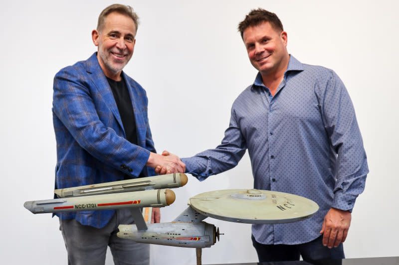 Heritage Auctions Executive Vice President Joe Maddalena (L) and Eugene “Rod” Roddenberry Jr., son of "Star Trek" creator Gene Roddenberry, shake hands in front of the starship Enterprise model used in the original series' opening credits. Photo by Josh David/Heritage Auctions