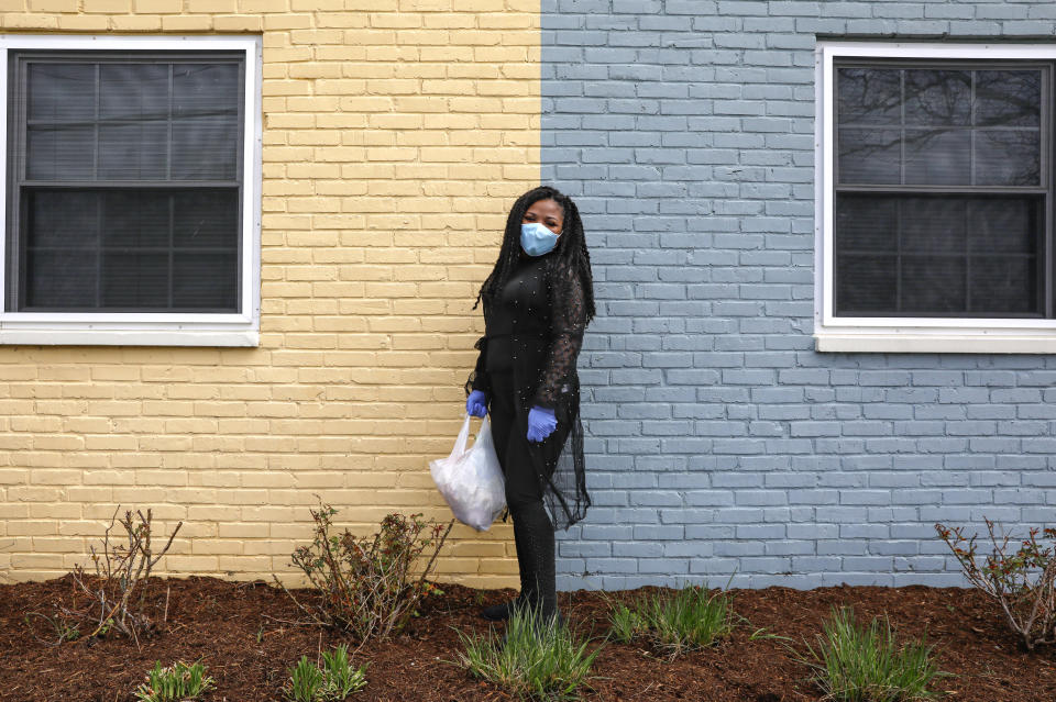 In this March 24, 2020, photo, Sharita Creel, of Washington, poses for a portrait holding a donated bag of groceries that she received in her community while wearing a mask and gloves in southeast Washington. Creel received the groceries from a neighborhood food delivery that is part of a new Martha's Table initiative, along with community partners, to get needed food directly to the neighborhoods they serve. Neighborhood volunteers are the tip of the spear for a grassroots community effort to keep Washington's most vulnerable neighborhoods fed during the unprecedented coronavirus crisis which has nearly shut down the American economy. (AP Photo/Jacquelyn Martin)