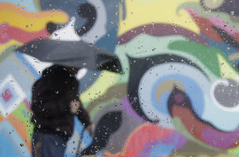 Rain drops are shown on a window as a man walks past a mural in San Francisco, Wednesday, March 6, 2019. Drenching rain is causing roadway flooding and traffic accidents as another storm pounds California. (AP Photo/Jeff Chiu)