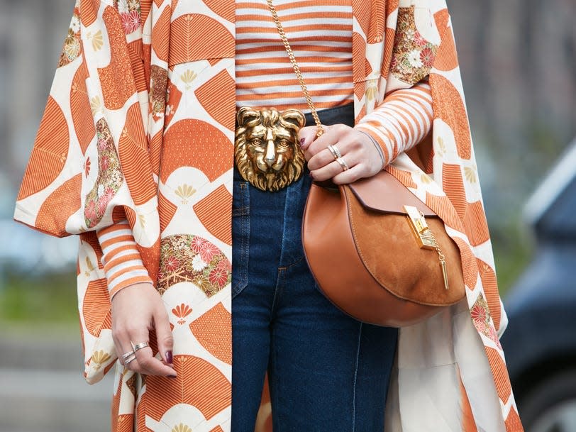woman wearing a orange striped shirt with a big lion head belt and jeans under a flowy orange printed jacket