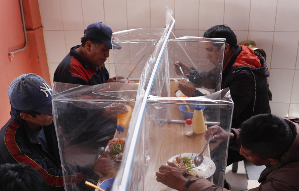 People eat lunch at a popular dining room with wood and plastic separations fitted to curb the spread of the coronavirus, at the Yungas market in La Paz, Bolivia, Tuesday, Sept. 22, 2020. Authorities from the Mayor's Office of La Paz authorized the opening of popular dining rooms with dividing panels on their tables, as a precautionary measure against COVID-19. (AP Photo/Juan Karita)