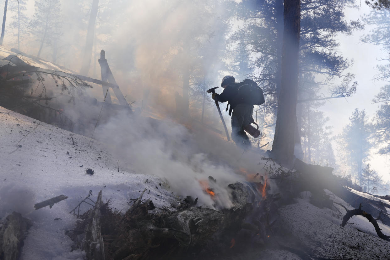 A member of the Mile High Youth Corps walks near a smoldering pile of tree debris during a controlled burn with the U.S. Forest Service in Hatch Gulch Wednesday, Feb. 23, 2022, near Deckers, Colo. (AP Photo/Brittany Peterson)