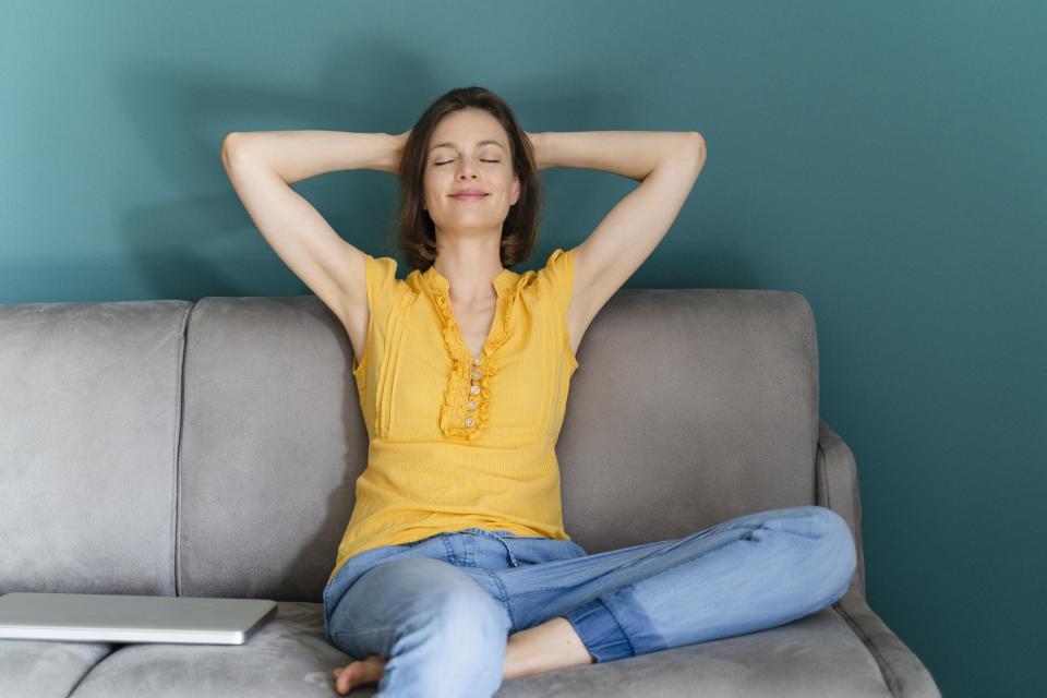 Woman relaxing with eyes closed and arms behind her head with her laptop shut nearby. 