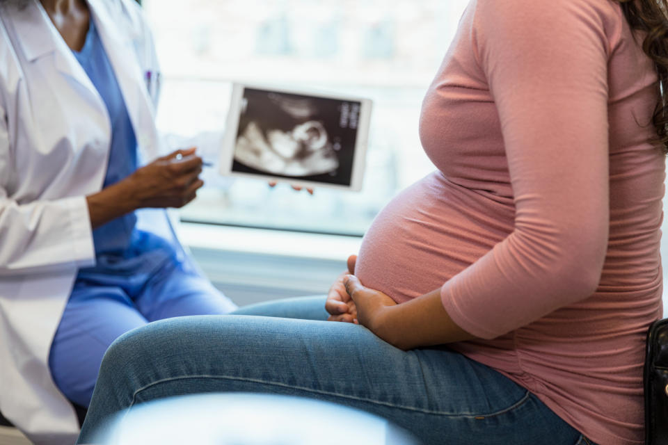 A pregnant person is holding their belly while a healthcare professional shows them an ultrasound image