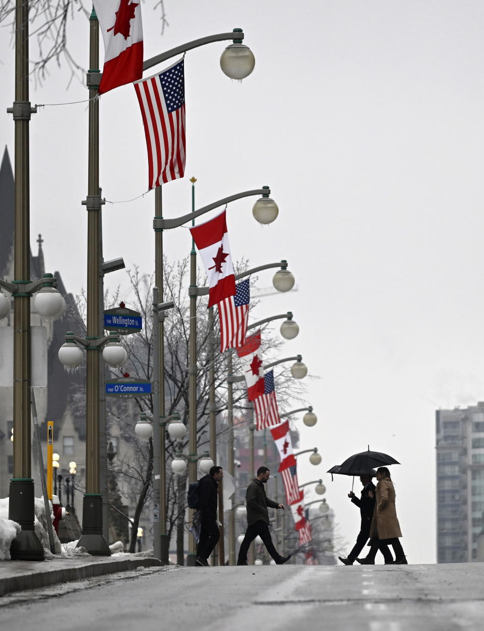 People hold umbrellas as they pass Canadian and American flags lining Wellington Street in front of Parliament Hill in Ottawa, before the visit of U.S. President Joe Biden to Canada, on Thursday, March 23, 2023. (Justin Tang /The Canadian Press via AP)