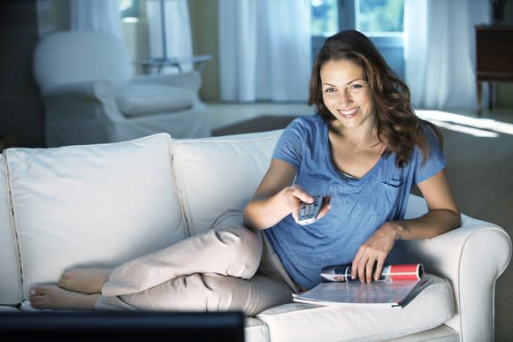 A woman watches TV on the couch.