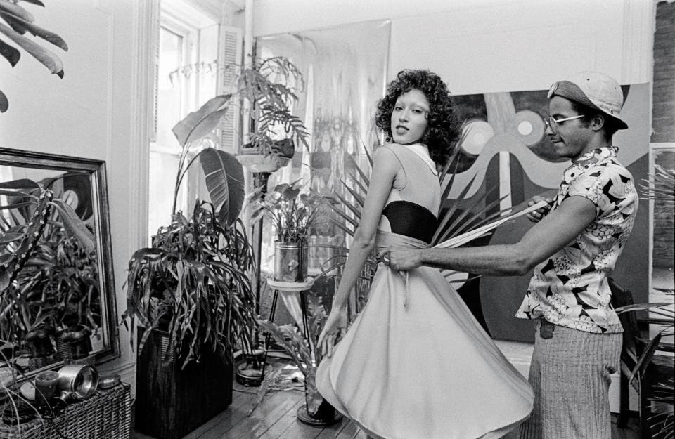 Designer Stephen Burrows fits a wrap dress on model and muse Pat Cleveland,  from his Fall 1971 collection at the designer's Greenwich Village apartment.  This is the first time the wrap dress is introduced at fashion retail.  From Black in Fashion, published by Union Square & Co. in 2024.  Photo by Pierre Schermann, courtesy WWD/Fairchild Media.