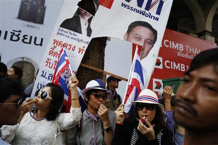 Under a damaged pre-election poster of Thai Prime Minister Yingluck Shinawatra, anti-government protesters blow whistles as they greet fellow demonstrators marching through Bangkok's financial district January 21, 2014. REUTERS/Damir Sagolj