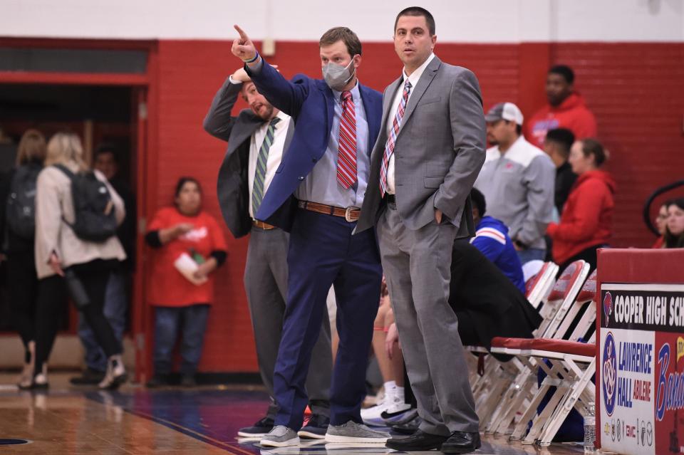 Cooper head coach Bryan Conover, left, Josh Alcorn, middle, and Michael Bacon look on from the bench while the Cougars play Wylie at Cougar Gym on Jan. 21, 2022. The Cougars led almost the entire game before pulling away late in the fourth quarter to win 54-41.