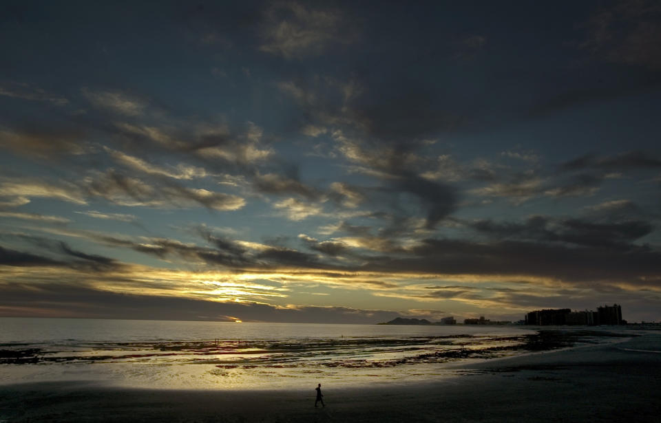 FILE - In this Sept. 27, 2007, file photo, a man walks alone on the beach during sunset in Puerto Penasco, Mexico. An unusual string of violence south of Arizona's border with Mexico has sparked travel warnings by American authorities and is forcing U.S. citizens who say they won't stop crossing into Mexico to at least consider how to travel more safely. (AP Photo/Guillermo Arias, File)