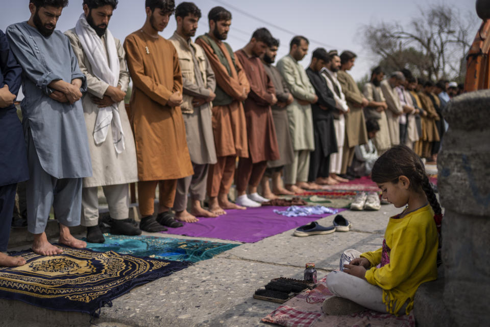 An Afghan girl working as a shoe cleaner sits in the street while men pray during Friday prayers in Kabul, Afghanistan, Friday, Sept. 24, 2021. (AP Photo/Bernat Armangue)