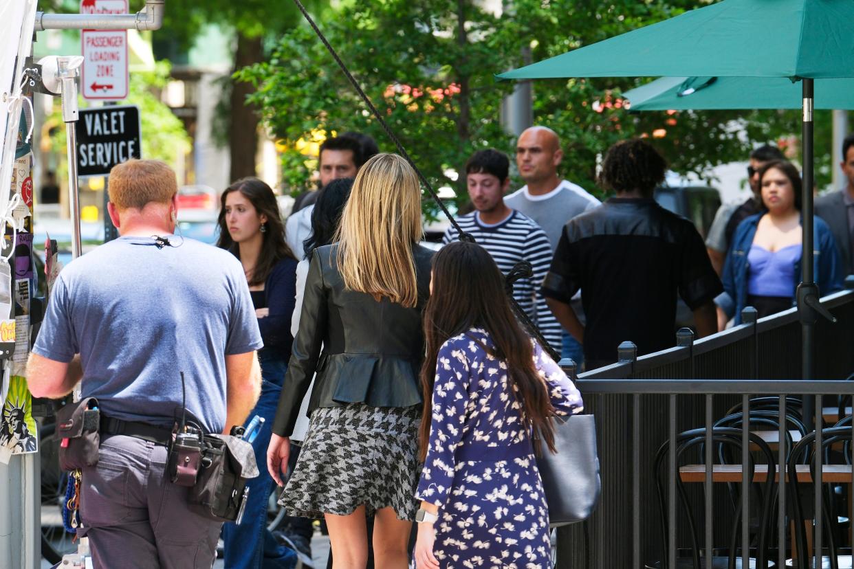 Extras walk back and forth on the sidewalk of Park Ave in May as background for a scene inside the coffee shop for the movie "Twisters."