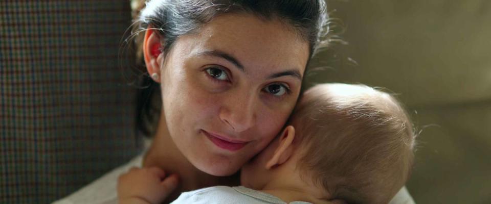 Mother holding baby smiling to camera. Real life authentic casual mom looking to camera holding sleeping infant