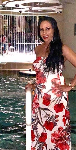 Abeni Mayfield in a red floral dress stands next to an indoor pool