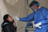 A healthcare worker takes a swab sample from a young woman's throat to test for COVID-19, in Mexico City, Saturday, July 10, 2021. Mexico is entering its third wave of the coronavirus pandemic. The country's health department said Friday the growth is largely coming from infections among younger, less vulnerable people. Macias tested negative. (AP Photo/Ginnette Riquelme)