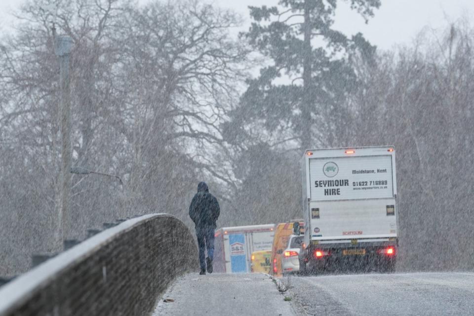 A pedestrian crosses a bridge during a snow shower near Maidstone (PA)
